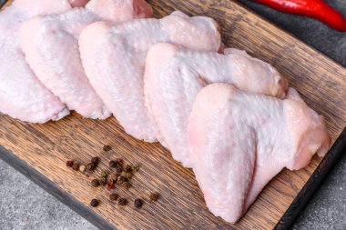 Raw chicken wings with ingredients for cooking on a wooden cutting board over gray slate