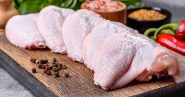 Raw chicken wings with ingredients for cooking on a wooden cutting board over gray slate