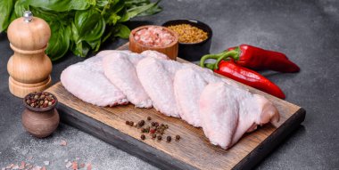 Raw chicken wings with ingredients for cooking on a wooden cutting board over gray slate
