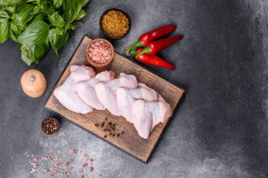 Raw chicken wings with ingredients for cooking on a wooden cutting board over gray slate