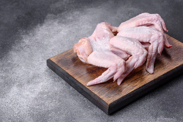 Raw chicken wings with ingredients for cooking on a wooden cutting board over gray slate