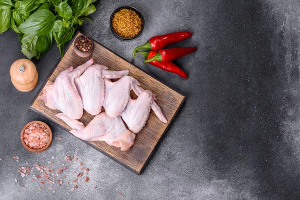 Raw chicken wings with ingredients for cooking on a wooden cutting board over gray slate