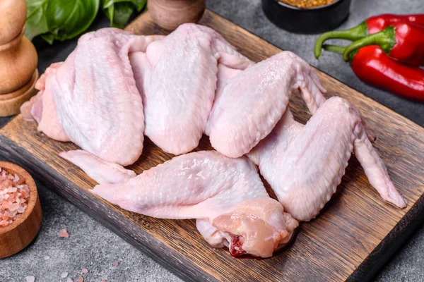 Raw chicken wings with ingredients for cooking on a wooden cutting board over gray slate