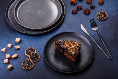 A piece of fresh delicious cake with nuts and chocolate on a black plate against a dark blue background. Desserts and sweets to the dinner table