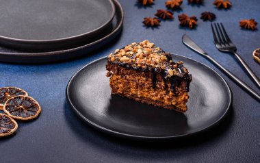 A piece of fresh delicious cake with nuts and chocolate on a black plate against a dark blue background. Desserts and sweets to the dinner table