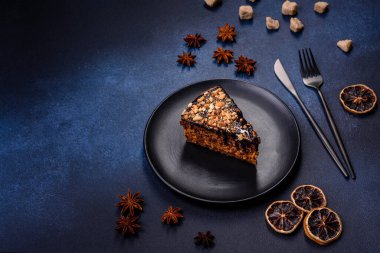 A piece of fresh delicious cake with nuts and chocolate on a black plate against a dark blue background. Desserts and sweets to the dinner table