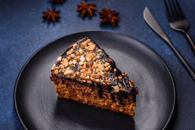 A piece of fresh delicious cake with nuts and chocolate on a black plate against a dark blue background. Desserts and sweets to the dinner table