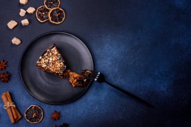 A piece of fresh delicious cake with nuts and chocolate on a black plate against a dark blue background. Desserts and sweets to the dinner table