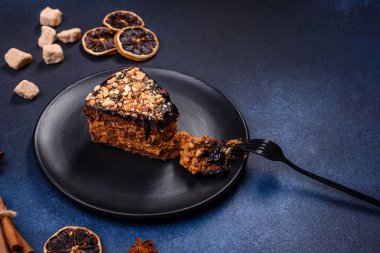 A piece of fresh delicious cake with nuts and chocolate on a black plate against a dark blue background. Desserts and sweets to the dinner table