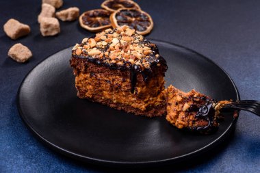 A piece of fresh delicious cake with nuts and chocolate on a black plate against a dark blue background. Desserts and sweets to the dinner table