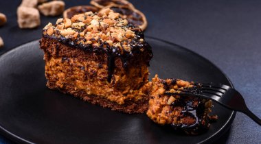 A piece of fresh delicious cake with nuts and chocolate on a black plate against a dark blue background. Desserts and sweets to the dinner table