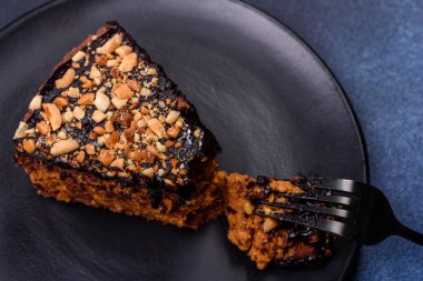 A piece of fresh delicious cake with nuts and chocolate on a black plate against a dark blue background. Desserts and sweets to the dinner table