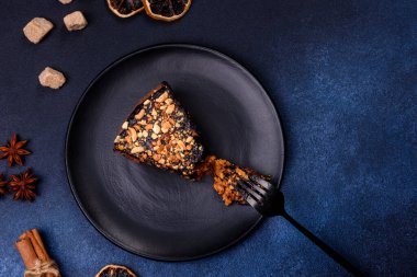 A piece of fresh delicious cake with nuts and chocolate on a black plate against a dark blue background. Desserts and sweets to the dinner table
