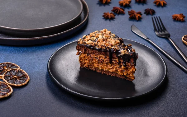 A piece of fresh delicious cake with nuts and chocolate on a black plate against a dark blue background. Desserts and sweets to the dinner table
