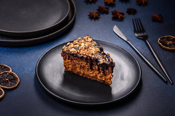 A piece of fresh delicious cake with nuts and chocolate on a black plate against a dark blue background. Desserts and sweets to the dinner table
