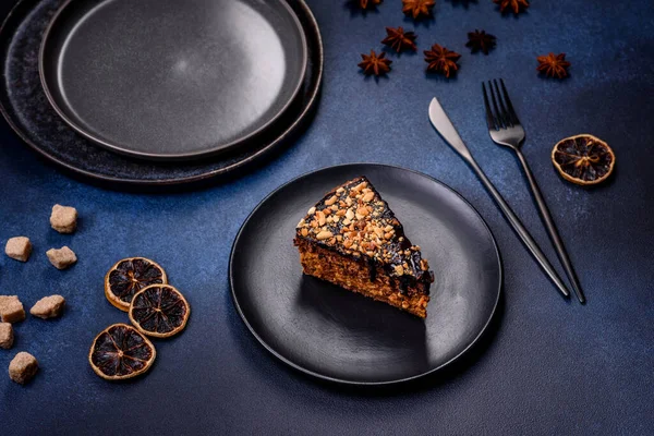 A piece of fresh delicious cake with nuts and chocolate on a black plate against a dark blue background. Desserts and sweets to the dinner table