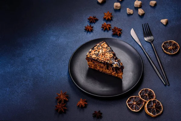 A piece of fresh delicious cake with nuts and chocolate on a black plate against a dark blue background. Desserts and sweets to the dinner table