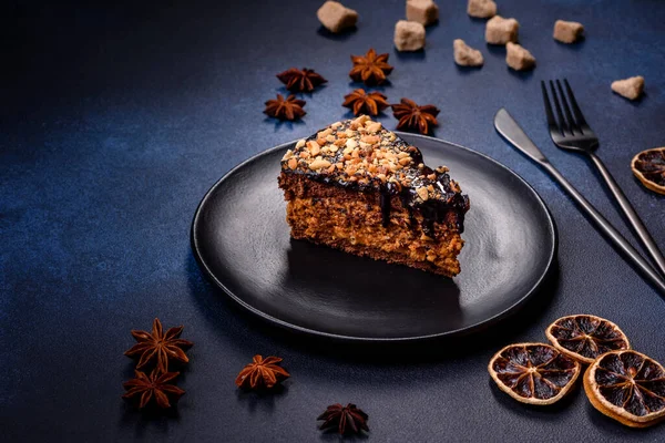 A piece of fresh delicious cake with nuts and chocolate on a black plate against a dark blue background. Desserts and sweets to the dinner table