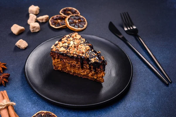 A piece of fresh delicious cake with nuts and chocolate on a black plate against a dark blue background. Desserts and sweets to the dinner table