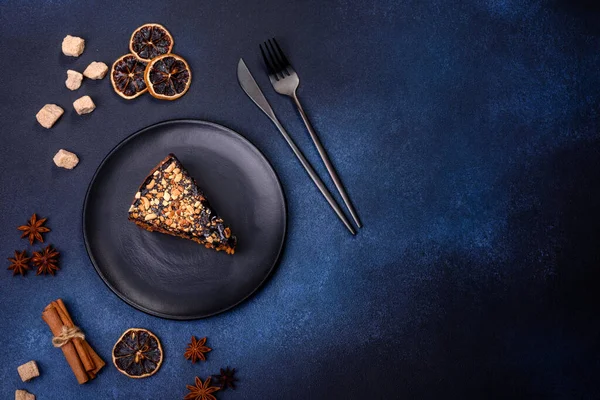 A piece of fresh delicious cake with nuts and chocolate on a black plate against a dark blue background. Desserts and sweets to the dinner table