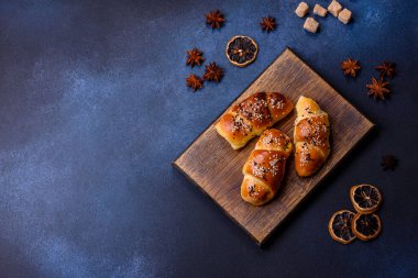 Delicious homemade pastries with apricot jam sprinkled with sesame seeds on a wooden cutting board against a blue concrete background