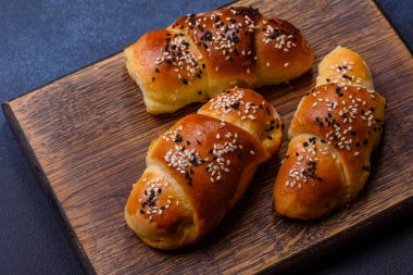 Delicious homemade pastries with apricot jam sprinkled with sesame seeds on a wooden cutting board against a blue concrete background