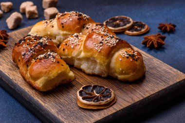 Delicious homemade pastries with apricot jam sprinkled with sesame seeds on a wooden cutting board against a blue concrete background