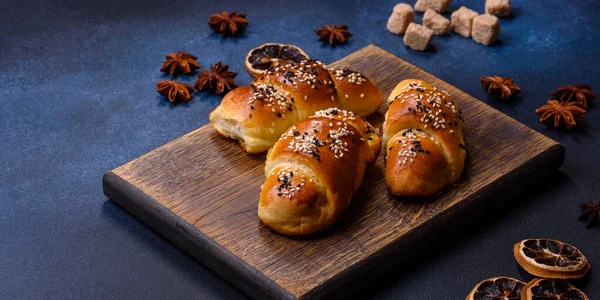Delicious homemade pastries with apricot jam sprinkled with sesame seeds on a wooden cutting board against a blue concrete background
