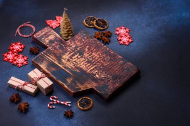 Elements of Christmas decorations, sweets and gingerbread on a wooden cutting board against a dark concrete background. Preparing for the holiday