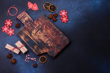 Elements of Christmas decorations, sweets and gingerbread on a wooden cutting board against a dark concrete background. Preparing for the holiday