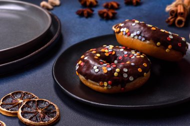 Pastries concept. Donuts with chocolate glaze with sprinkles, on a dark concrete table. Sweet food for a breakfast