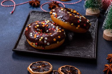 Pastries concept. Donuts with chocolate glaze with sprinkles, on a dark concrete table. Sweet food for a breakfast