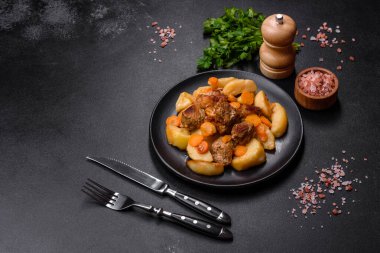 Beef meat and vegetables stew on a black plate with roasted potatoes. Dark background. Copy space