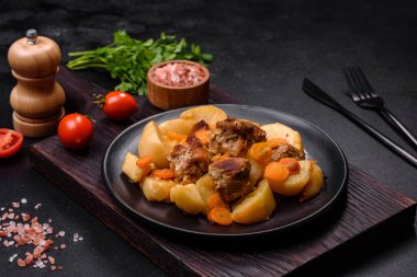 Beef meat and vegetables stew on a black plate with roasted potatoes. Dark background. Copy space