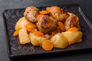 Beef meat and vegetables stew on a black plate with roasted potatoes. Dark background. Copy space