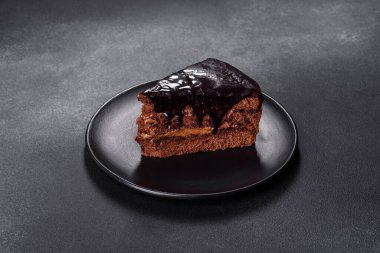 A piece of fresh delicious cake with nuts and chocolate on a black plate against a dark blue background. Desserts and sweets to the dinner table