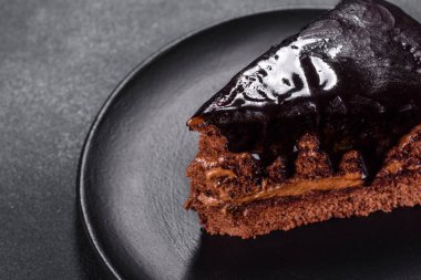 A piece of fresh delicious cake with nuts and chocolate on a black plate against a dark blue background. Desserts and sweets to the dinner table