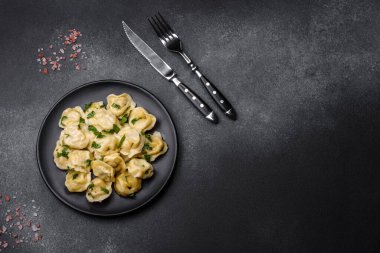 Delicious fresh dumplings with turkey meat, with spices and herbs, parsley on a black plate against a dark concrete background