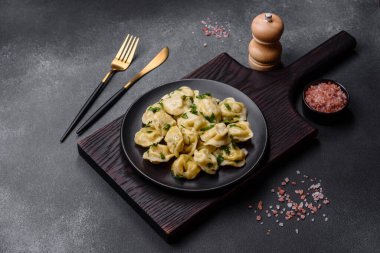 Delicious fresh dumplings with turkey meat, with spices and herbs, parsley on a black plate against a dark concrete background