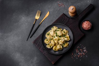 Delicious fresh dumplings with turkey meat, with spices and herbs, parsley on a black plate against a dark concrete background