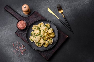 Delicious fresh dumplings with turkey meat, with spices and herbs, parsley on a black plate against a dark concrete background