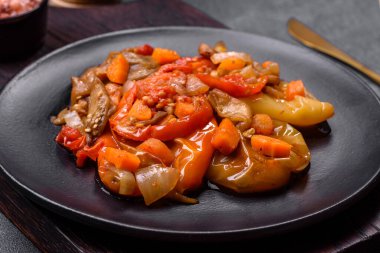 Baked vegetables, eggplant, peppers and carrots on a black plate on a gray concrete background. Vegetarian food