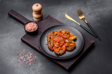 Baked vegetables, eggplant, peppers and carrots on a black plate on a gray concrete background. Vegetarian food