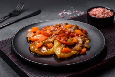 Baked vegetables, eggplant, peppers and carrots on a black plate on a gray concrete background. Vegetarian food