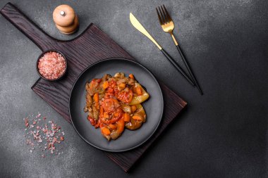 Baked vegetables, eggplant, peppers and carrots on a black plate on a gray concrete background. Vegetarian food