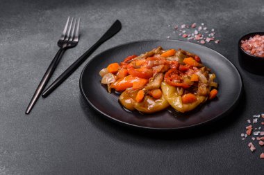 Baked vegetables, eggplant, peppers and carrots on a black plate on a gray concrete background. Vegetarian food