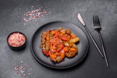 Baked vegetables, eggplant, peppers and carrots on a black plate on a gray concrete background. Vegetarian food