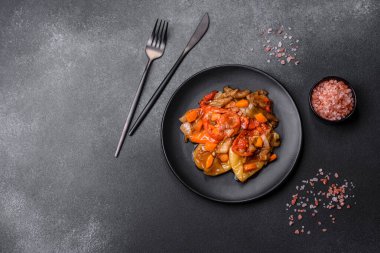 Baked vegetables, eggplant, peppers and carrots on a black plate on a gray concrete background. Vegetarian food