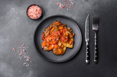 Baked vegetables, eggplant, peppers and carrots on a black plate on a gray concrete background. Vegetarian food
