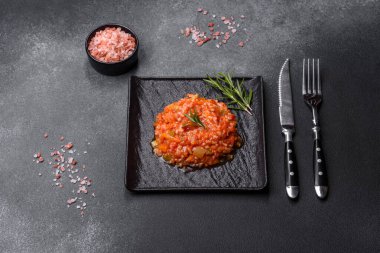 Boiled rice with peppers, spices, herbs and tomato sauce on a black slate plate on a grey concrete background